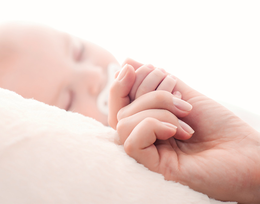 Primer plano de la mano de una mujer sosteniendo la mano de un bebé dormido