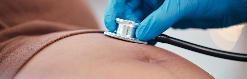 Mano de un médico con un guante azul colocando un estetoscopio en el abdomen de una mujer embarazada