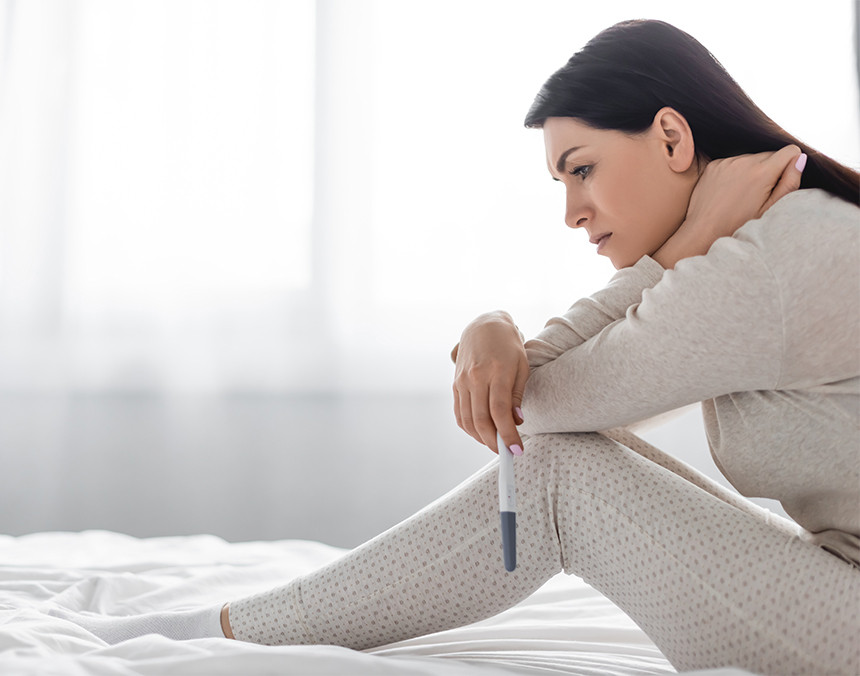 Mujer triste sentada en una cama, sosteniendo una prueba de embarazo
