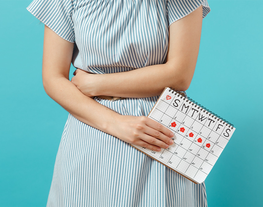 Mujer con dolor abdominal sosteniendo un calendario marcado con puntos de color rojo