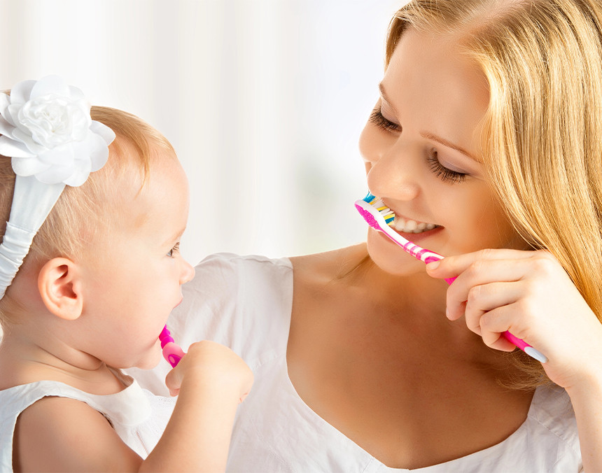 Mamá y bebé cepillándose los dientes juntas y mirándose fijamente