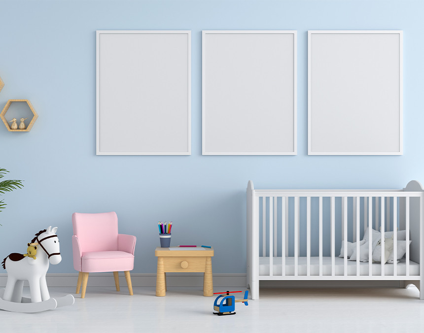 Cuarto de un bebé con una cuna blanca, tres cuadros blancos, un sillón rosa y un caballito de madera