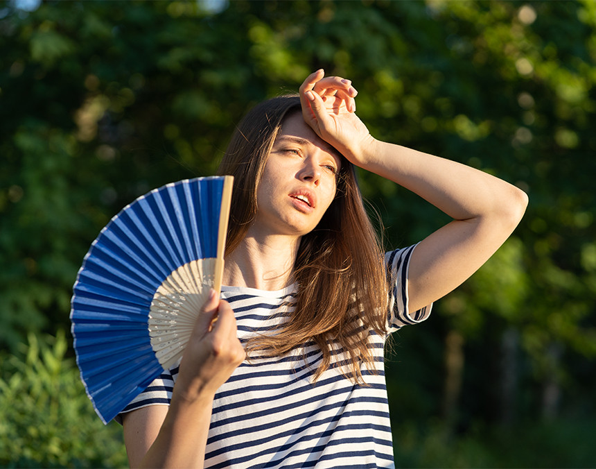 Mujer joven acalorada en un parque está sosteniendo un abanico de color azul