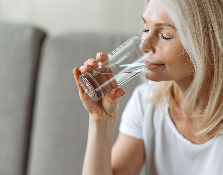Mujer joven con cabello rubio bebiendo agua simple de un vaso de vidirio