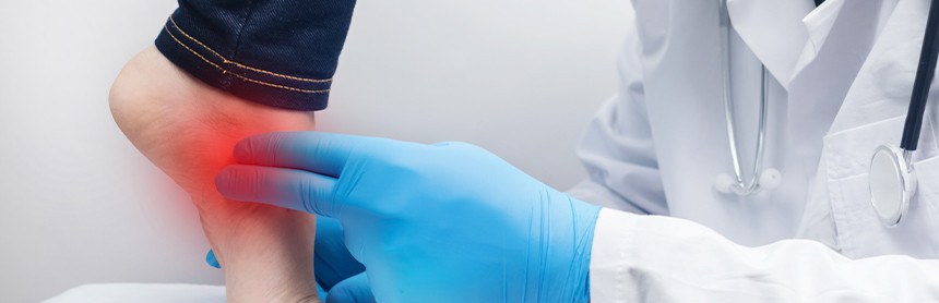 Médico con bata blanca y guantes azules examinando el pie de una paciente