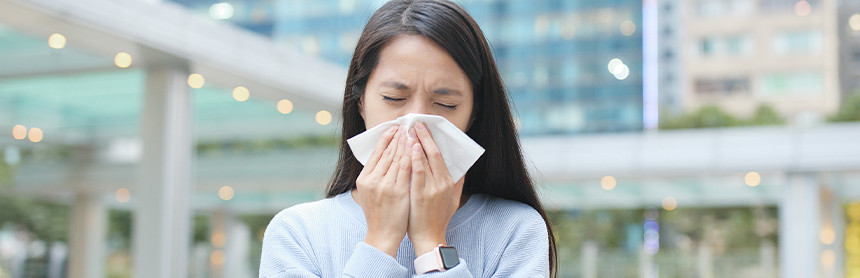 Mujer joven estornudando y cubriéndose con un pañuelo blanco