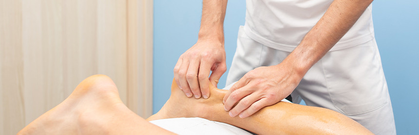 Fisioterapeuta con uniforme blanco realizando un masaje en el tendón de Aquiles de un paciente que se encuentra recostado