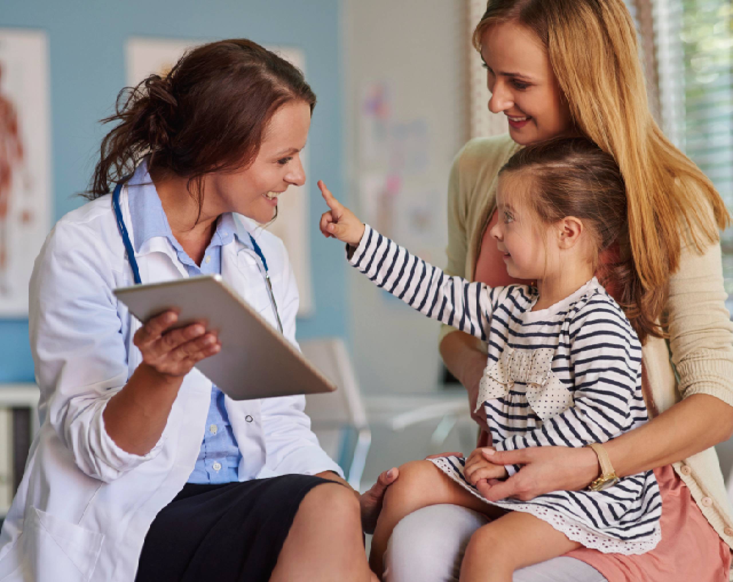 Niña paciente acompañada de su madre sentadas en el consultorio junto a la médica pediatra.