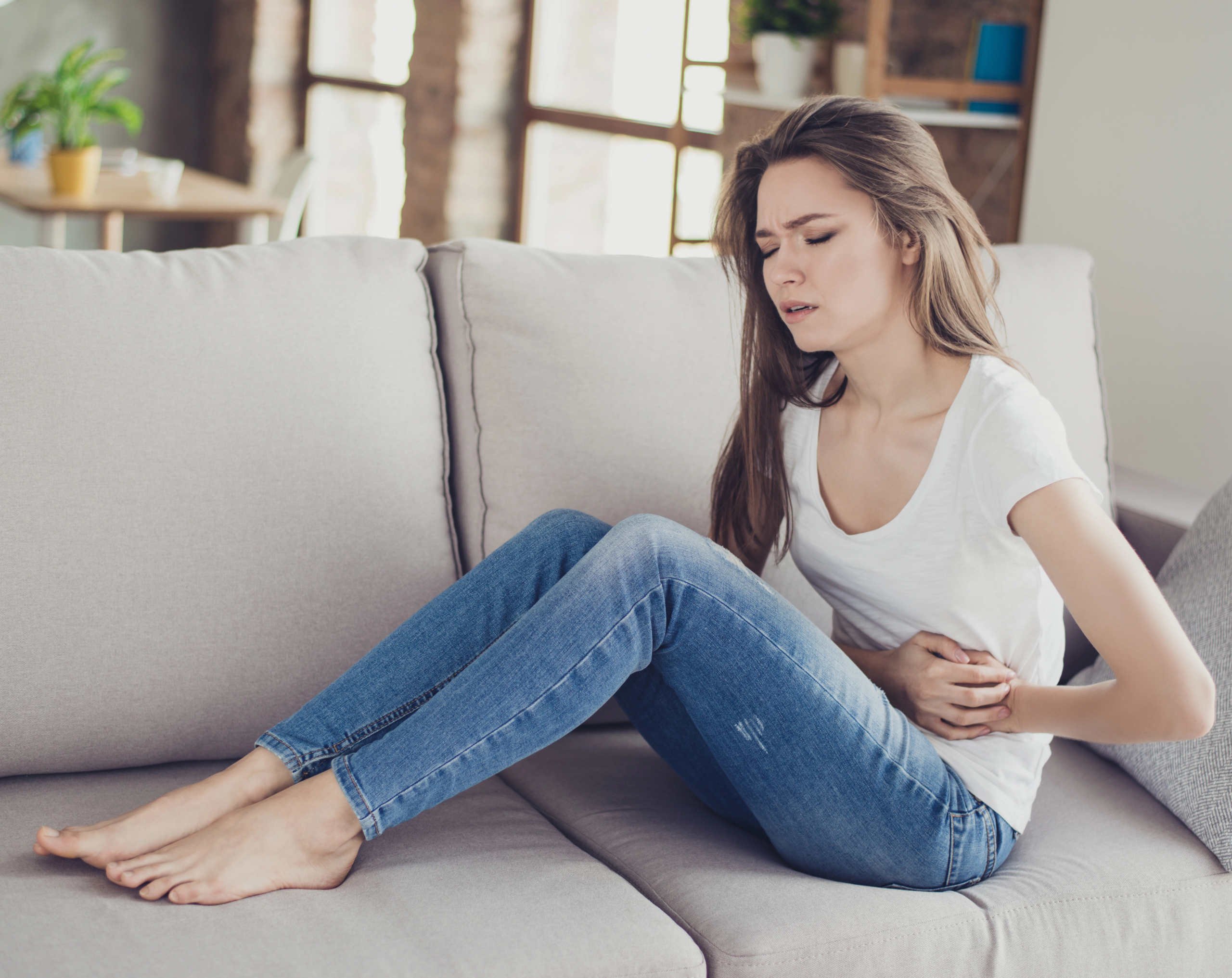 Mujer joven recostada con dolor abdominal, un síntoma de apendicitis.