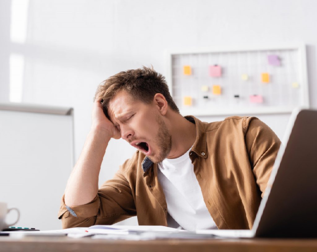 Hombre de edad joven bosteza durante horario laboral, como un síntoma de resistencia a la insulina.