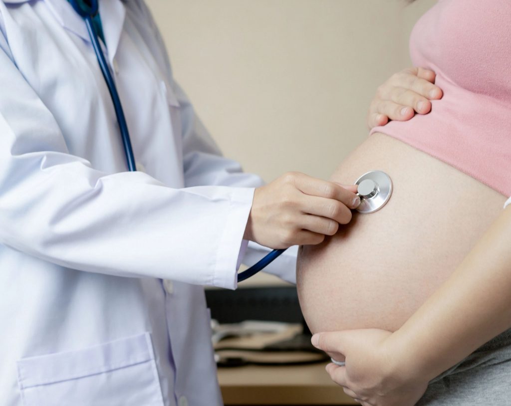 Ginecólogo coloca un estetoscopio sobre el vientre de una mujer embarazada durante una revisión prenatal para evaluar la salud del bebé ante un posible riesgo de transmisión del VIH.