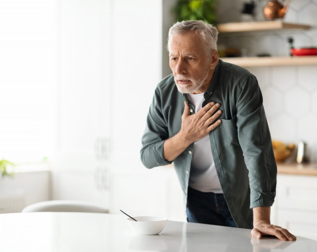 Hombre de tercera edad tocándose el pecho debido a un dolor del corazón, por posible infarto.
