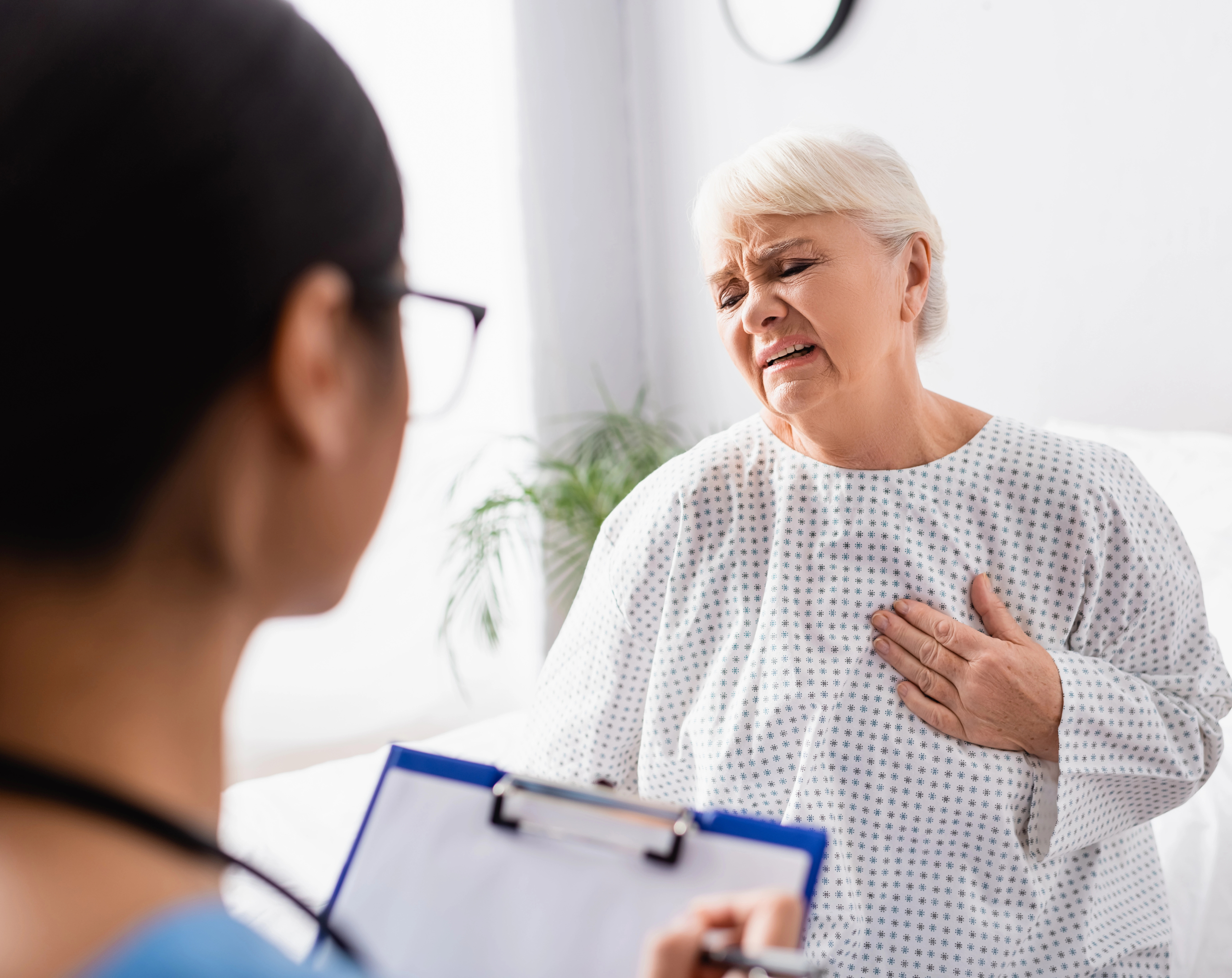Mujer de tercera edad hospitalizada por problemas del corazón, se toca el pecho por dolor, con riesgo de infarto.