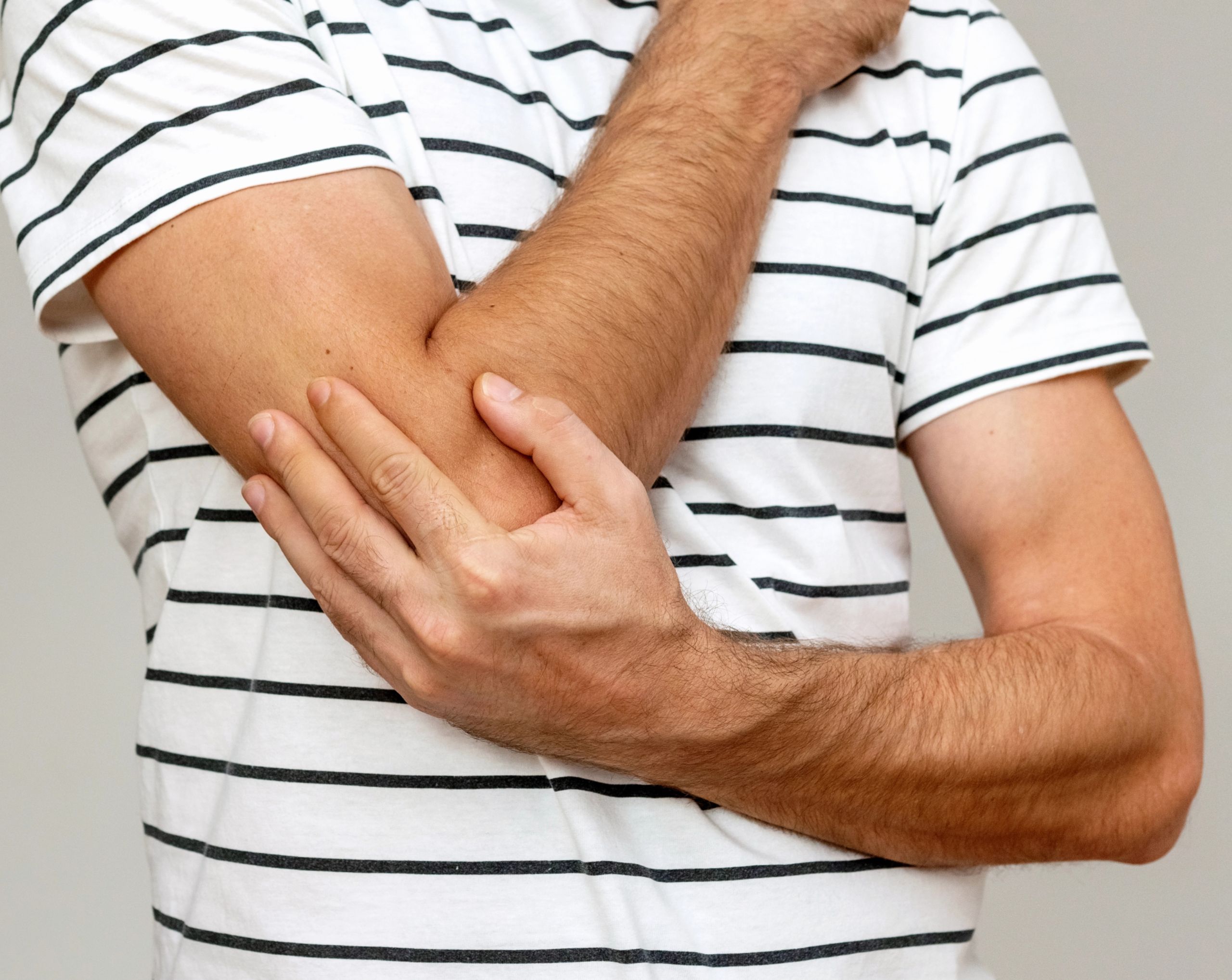Hombre de mediana edad sosteniendo su codo con la mano contraria debido al dolor causado por la epicondilitis o codo de tenista.