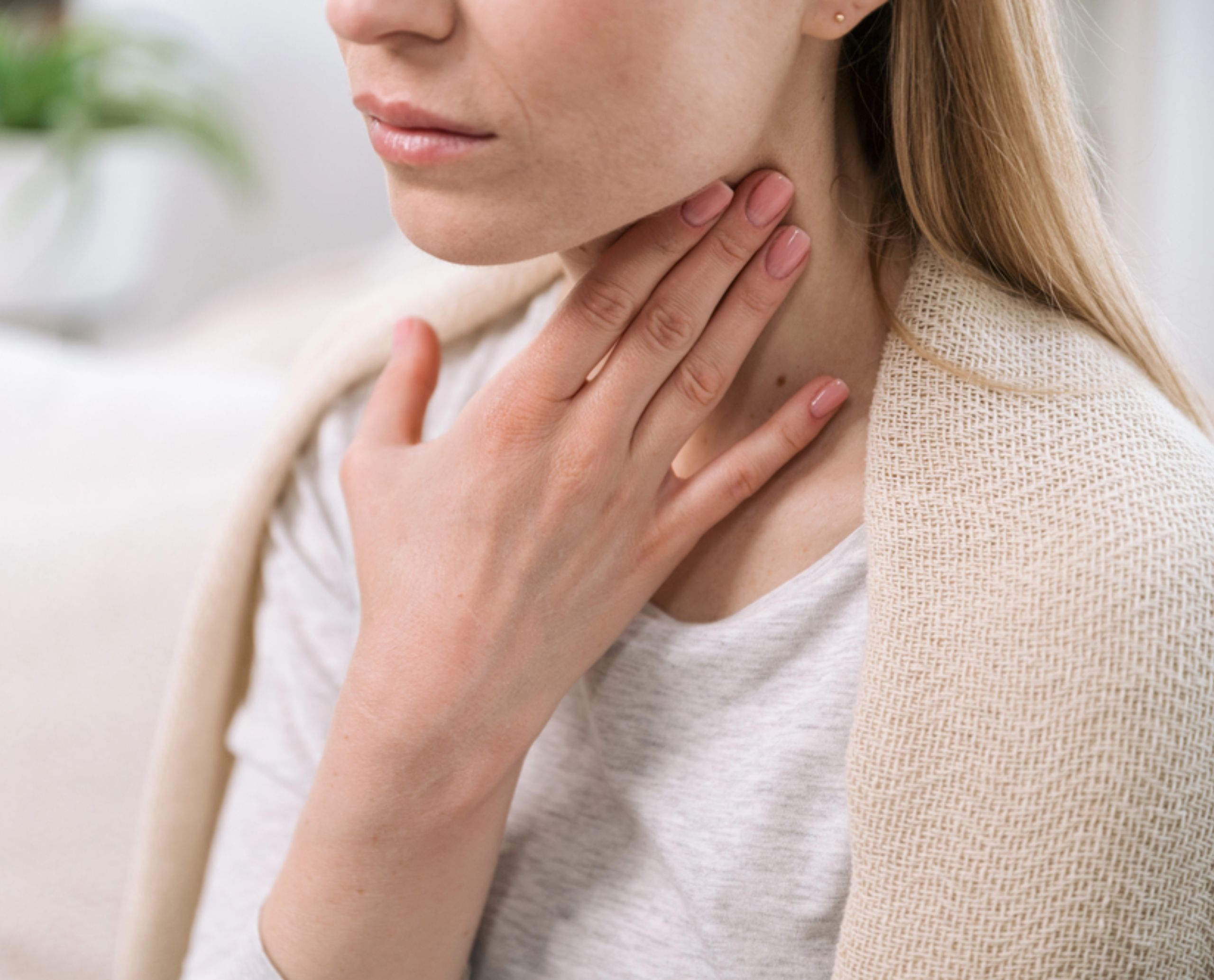 Mujer de mediana edad toca su garganta con una de sus manos por el dolor que le causa la amigdalitis.