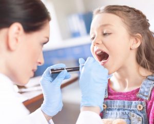 Médica pediatra examina las amígdalas de una niña para evaluar síntomas de amigdalitis.