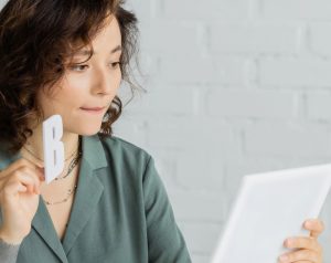 Mujer de mediana edad sostiene una letra “B” y una libreta durante una sesión de terapia del habla como parte del tratamiento para la hidrocefalia.