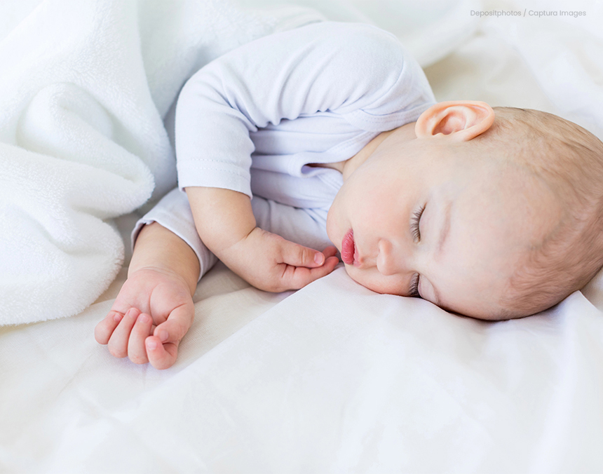 Bebé de pocos meses de edad durmiendo sobre una cama con sábanas blancas