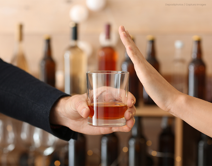 Mujer rechazando un vaso de whisky a un barman en un bar. Atrás hay diversas botellas de alcohol