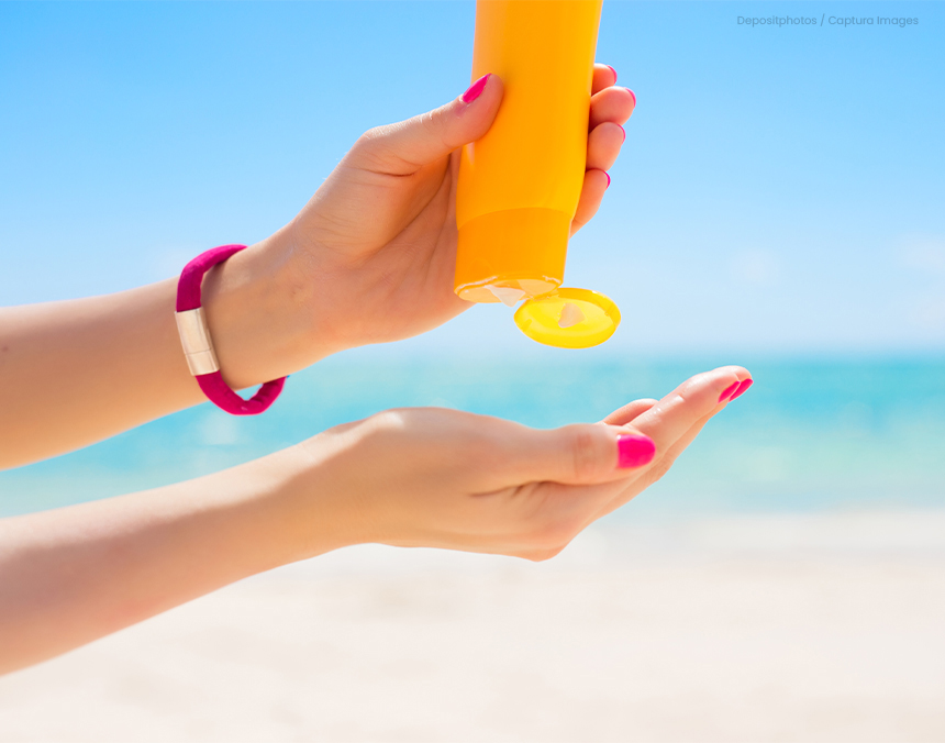 Manos de mujer con las uñas pintadas de rosa, aplicándose protector solar de una botella amarilla