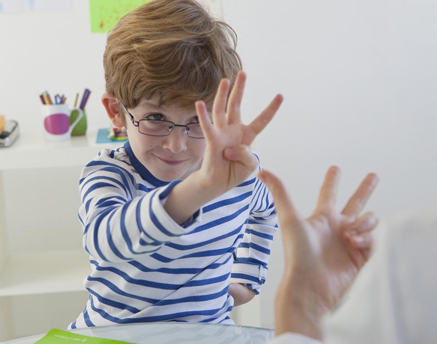 Niño sentado en un salón de clases, mostrando su mano a el adulto que esta frente de él.