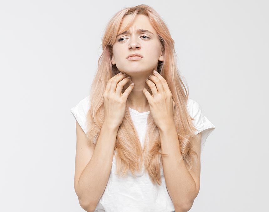 mujer rascándose el cuello, con cara de molestia y cabello rubio.