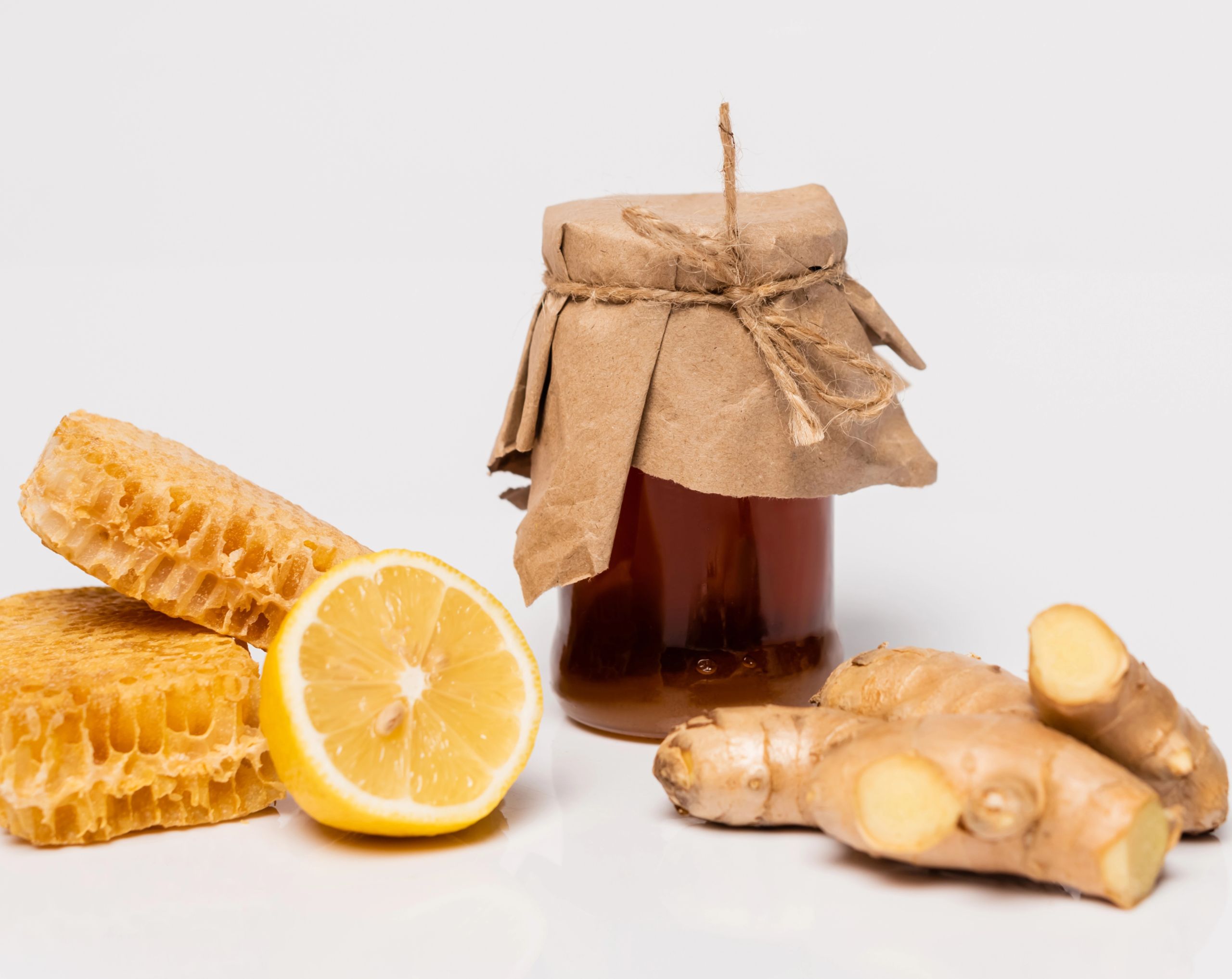 Frasco de miel junto a una rodaja de naranja y jengibre, remedios caseros que pueden ayudar a aliviar la tos.
