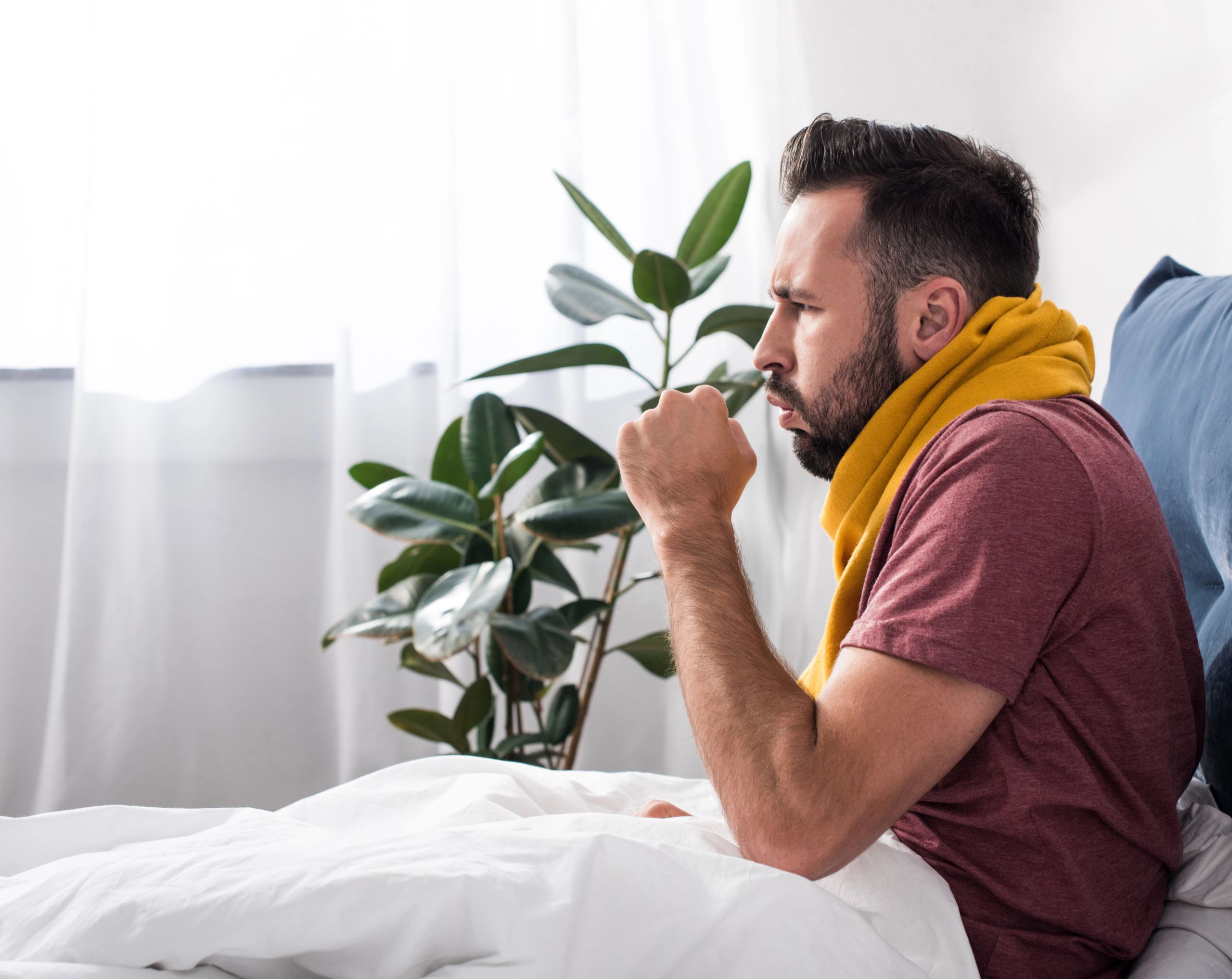 Hombre de mediana edad sentado en su cama mientras presenta tos persistente.