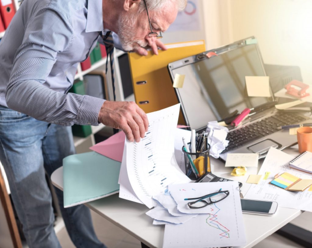 Hombre de edad media buscando documentos en un escritorio desorganizado, que muestra su diagnóstico de TDAH en adultos.