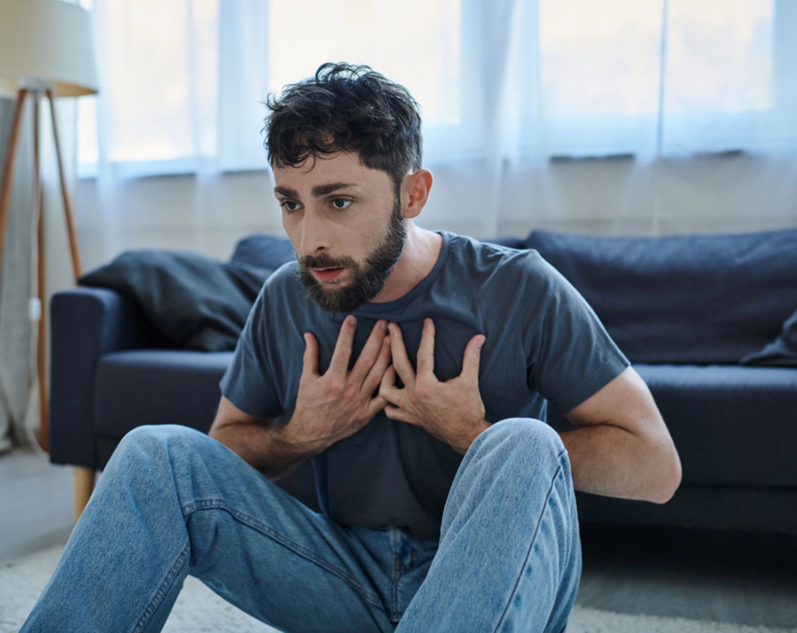Hombre con barba negra sentado en el piso mientras presenta síntomas asociados a la esquizofrenia. 