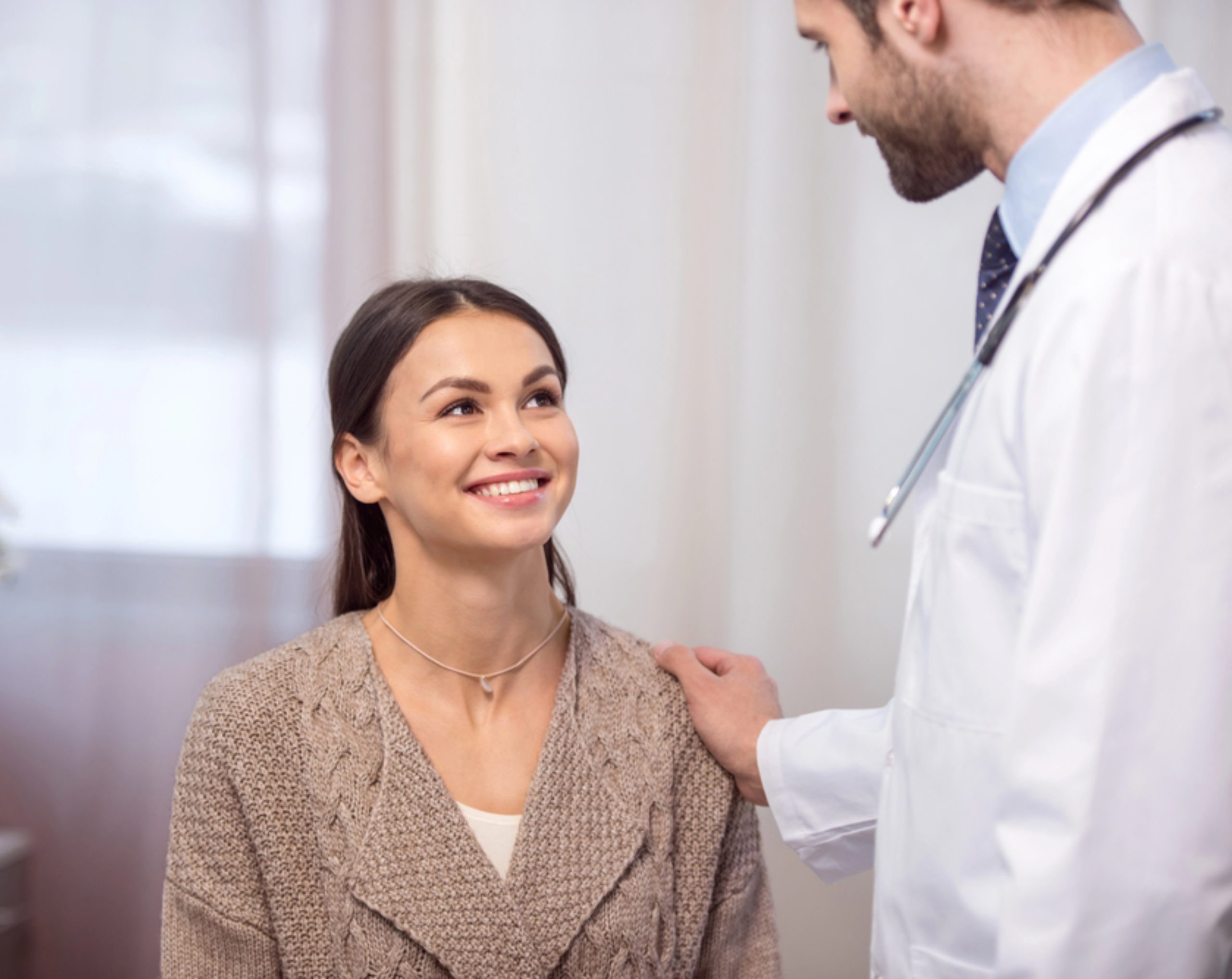 Mujer con suéter café conversando con un doctor con bata blanca en consultorio durante una consulta de valoración para determinar si puede realizar ayuno intermitente.