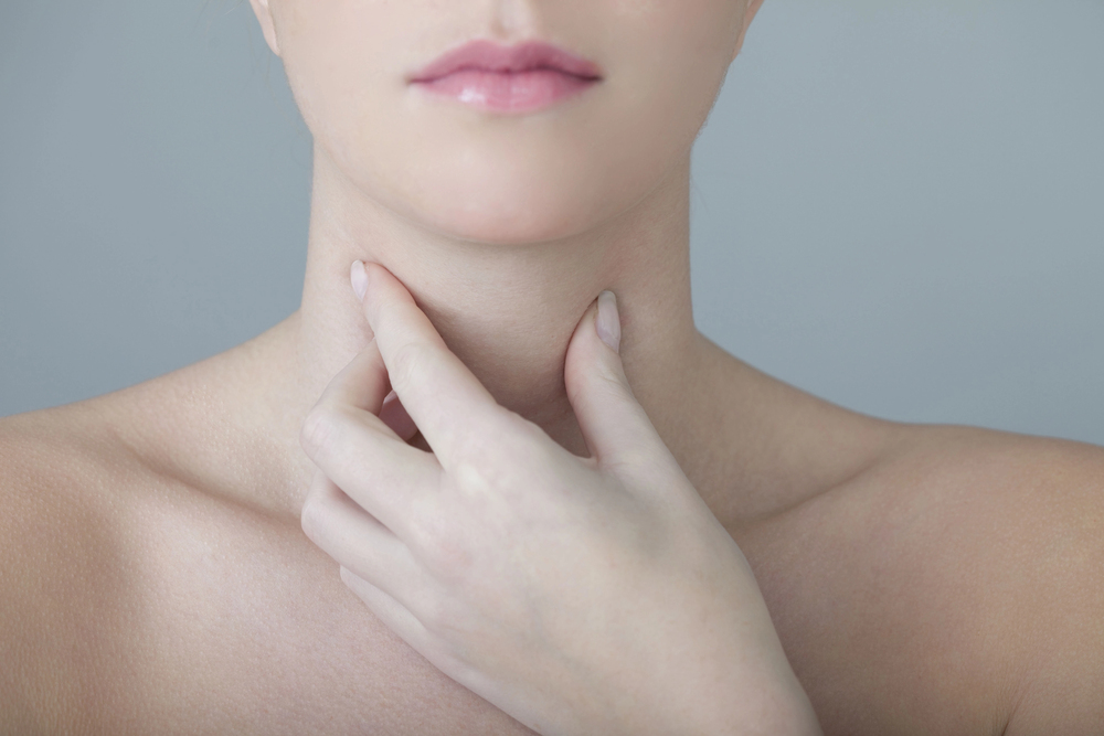 Mujer tocando su cuello por dolor o inflamación, ilustrando síntomas del cáncer de cabeza y cuello como dolor de garganta persistente, bultos e inflamación.  