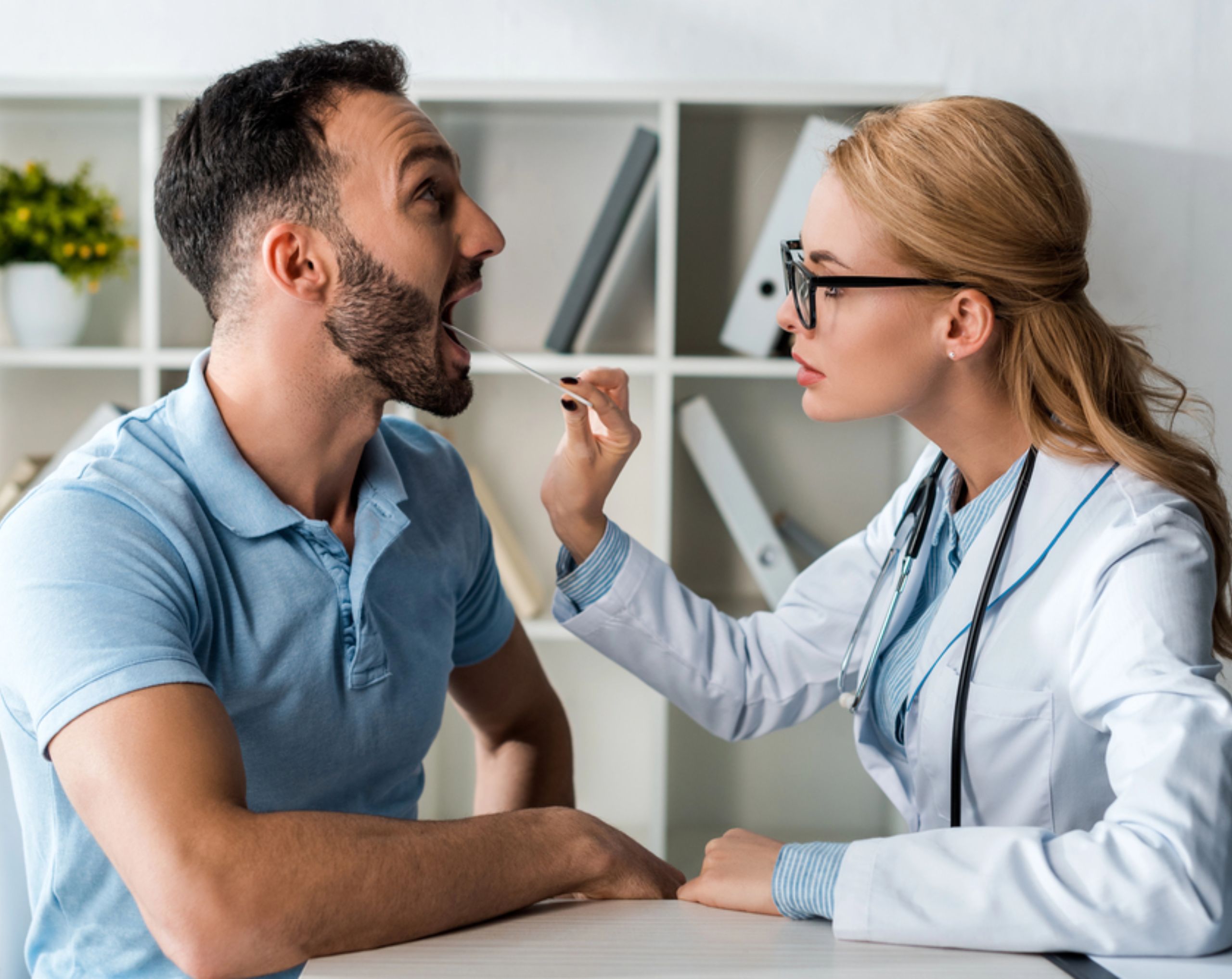 Doctora revisando la zona de laringe a paciente con síntomas de cáncer de cabeza y cuello en consulta médica.