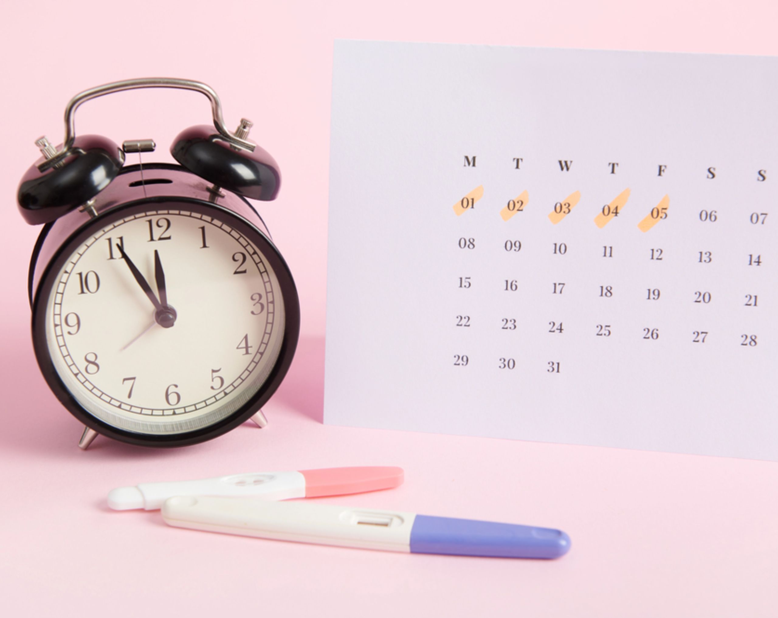 Reloj, calendario y una prueba de embarazo sobre una superficie, en representación del seguimiento del ciclo menstrual y los días fértiles.