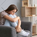 Mujer joven sentada en un sillón reflexiona con expresión seria, representando dificultad para expresar emociones, síntoma de alexitimia.