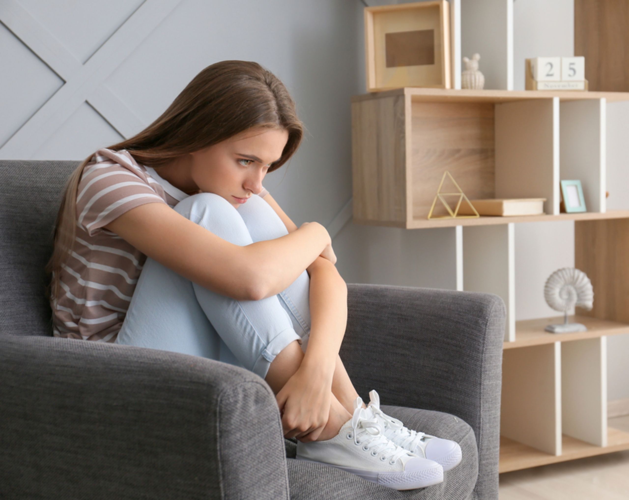 Mujer joven sentada en un sillón reflexiona con expresión seria, representando dificultad para expresar emociones, síntoma de alexitimia.
