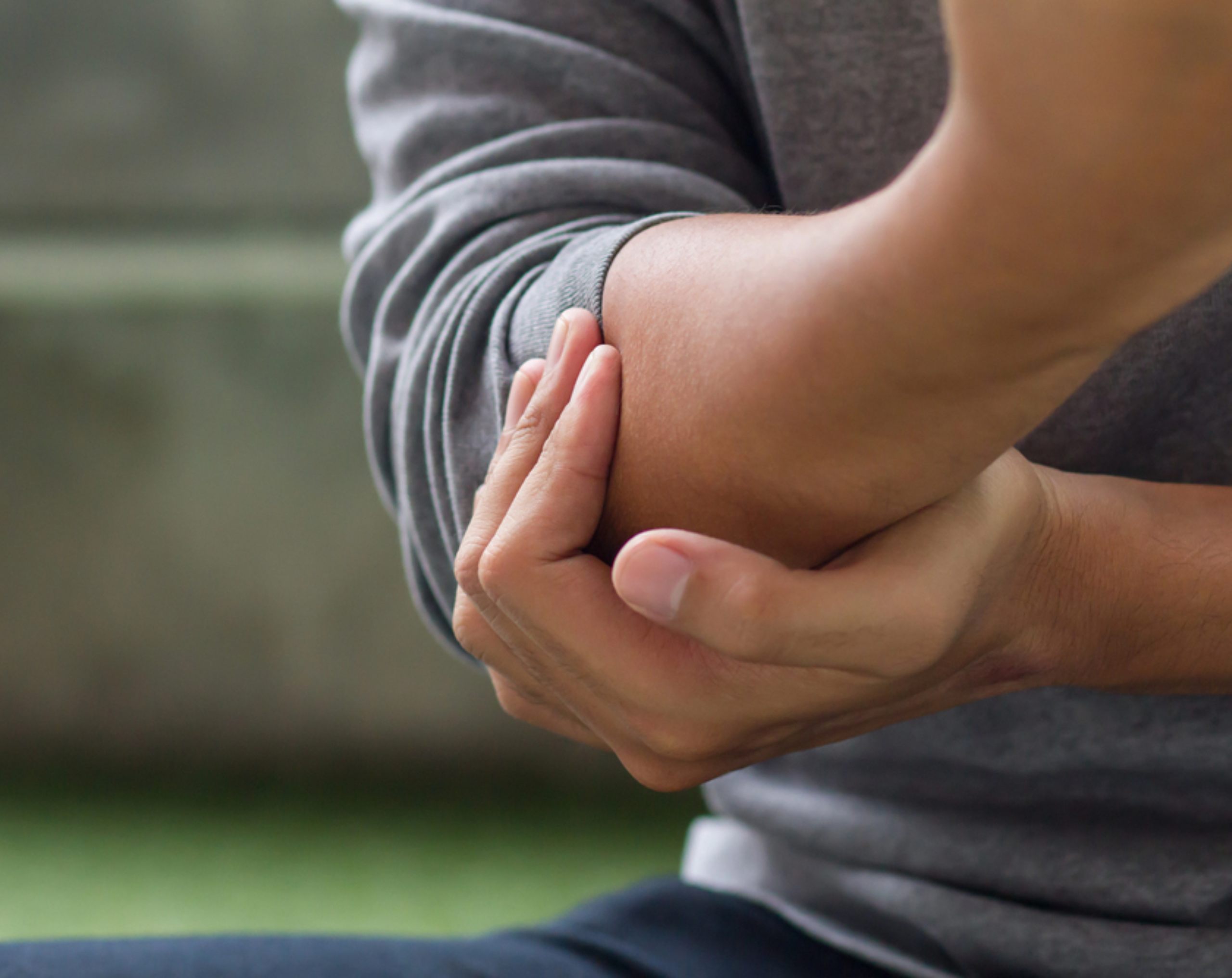 Hombre de mediana edad sujetando su codo izquierdo con la mano derecha debido al dolor causado por el codo de tenista