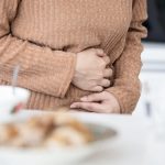 Persona adulta tocando su abdomen debido a dolor estomacal, posible síntoma de gastroenteritis.