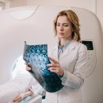 Médica sostiene una imagen de resonancia magnética cerebral mientras la paciente permanece recostada en el resonador.
