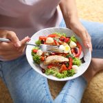 Mujer joven sosteniendo un plato con comida de dieta keto, rica en grasas saludables y baja en carbohidratos.