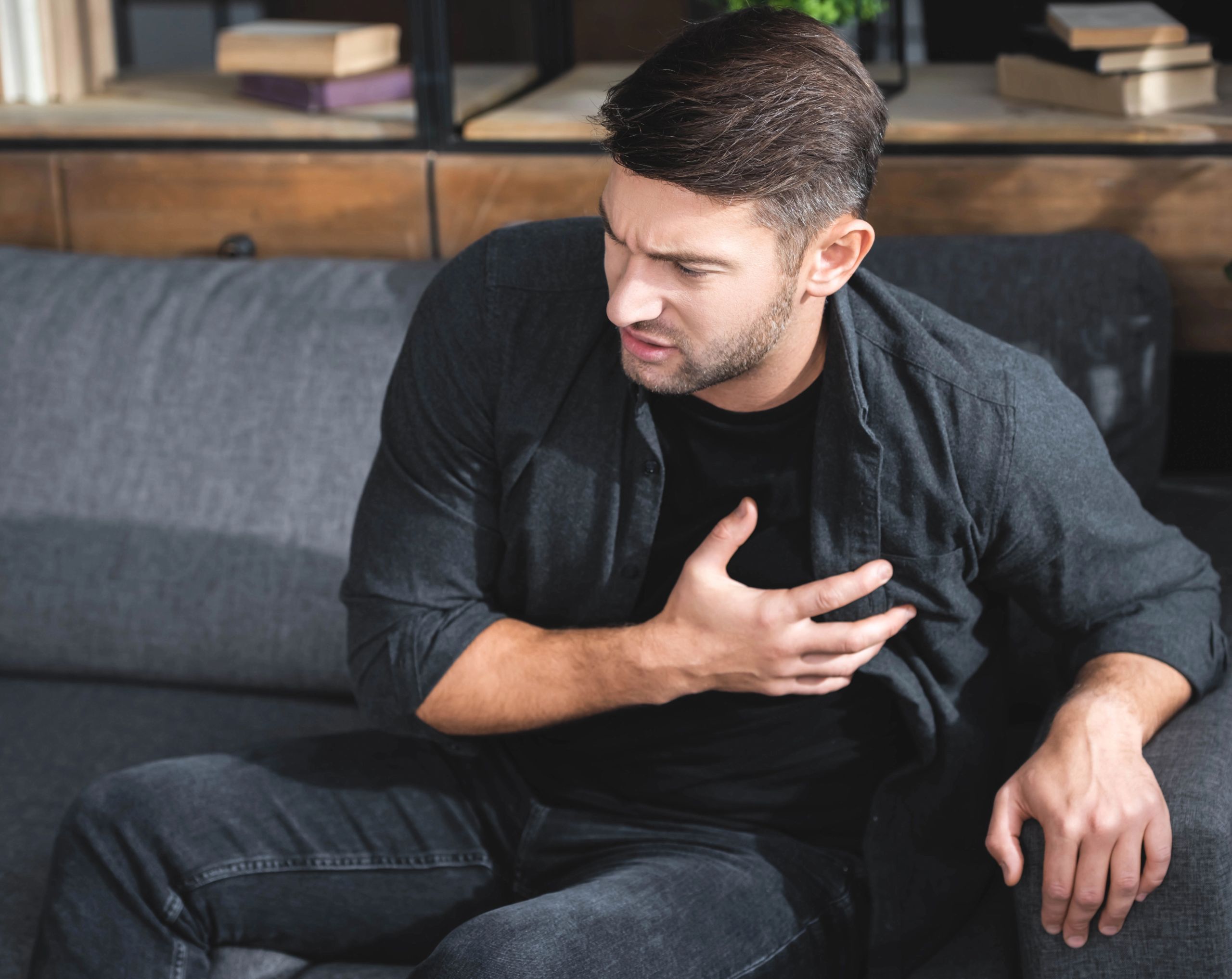 Hombre joven con la mano derecha sobre el pecho, a la altura del corazón, mostrando dolor como posible síntoma de miocardiopatía dilatada.