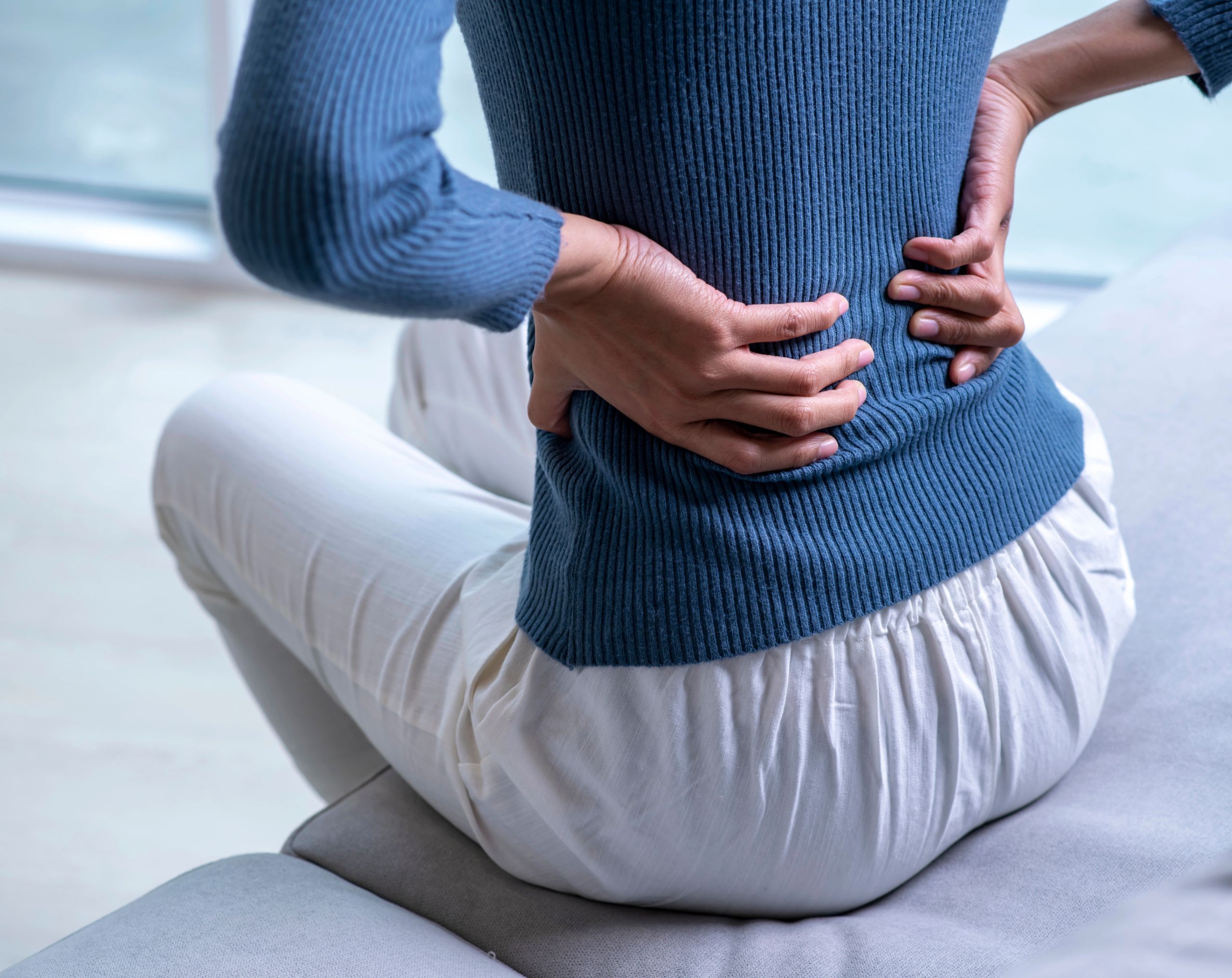 Mujer sentada en la cama, sosteniendo su espalda con ambas manos debido al dolor muscular, síntoma característico de la polimiositis.