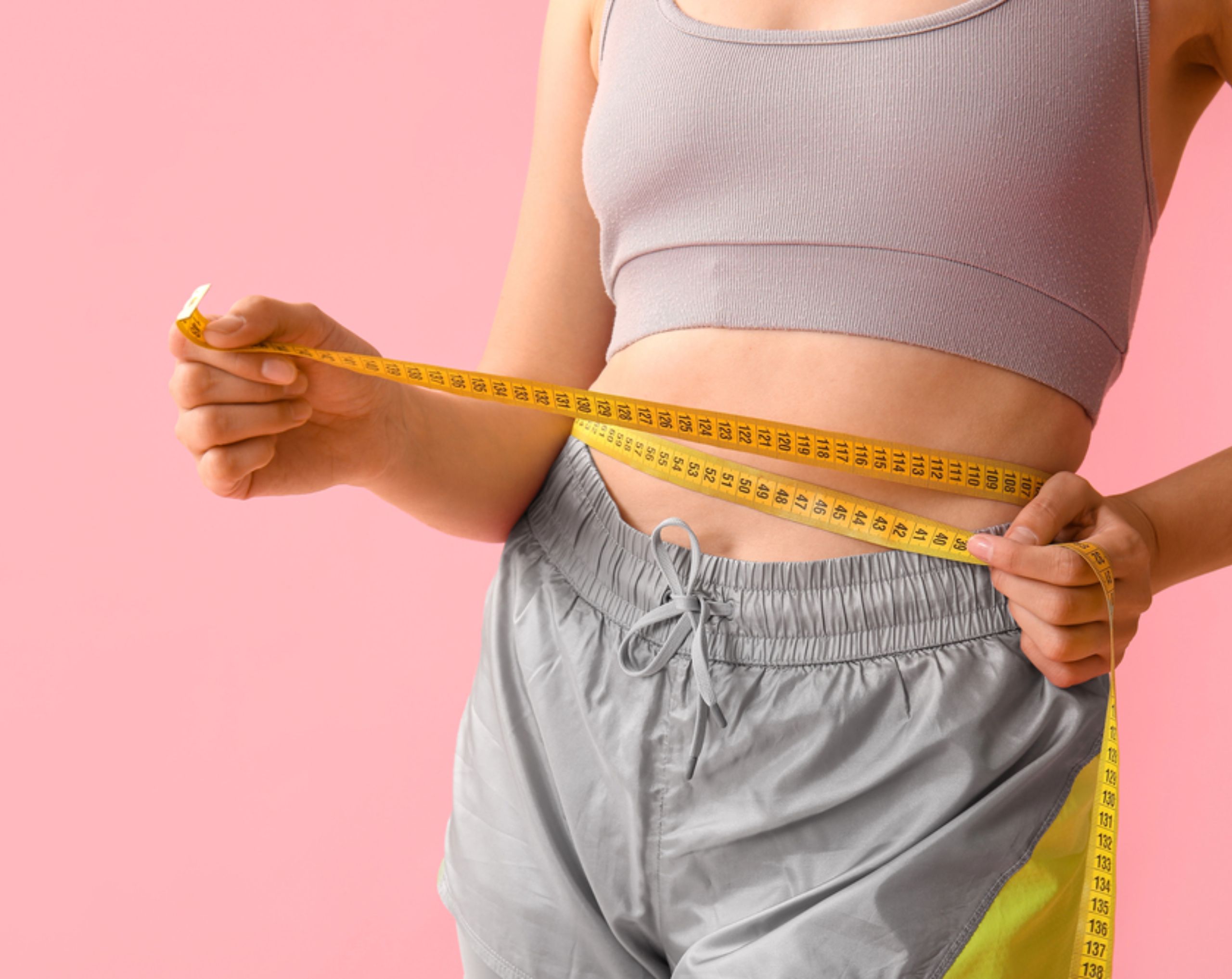 Mujer joven midiendo su cintura con una cinta métrica tras seguir una dieta keto.