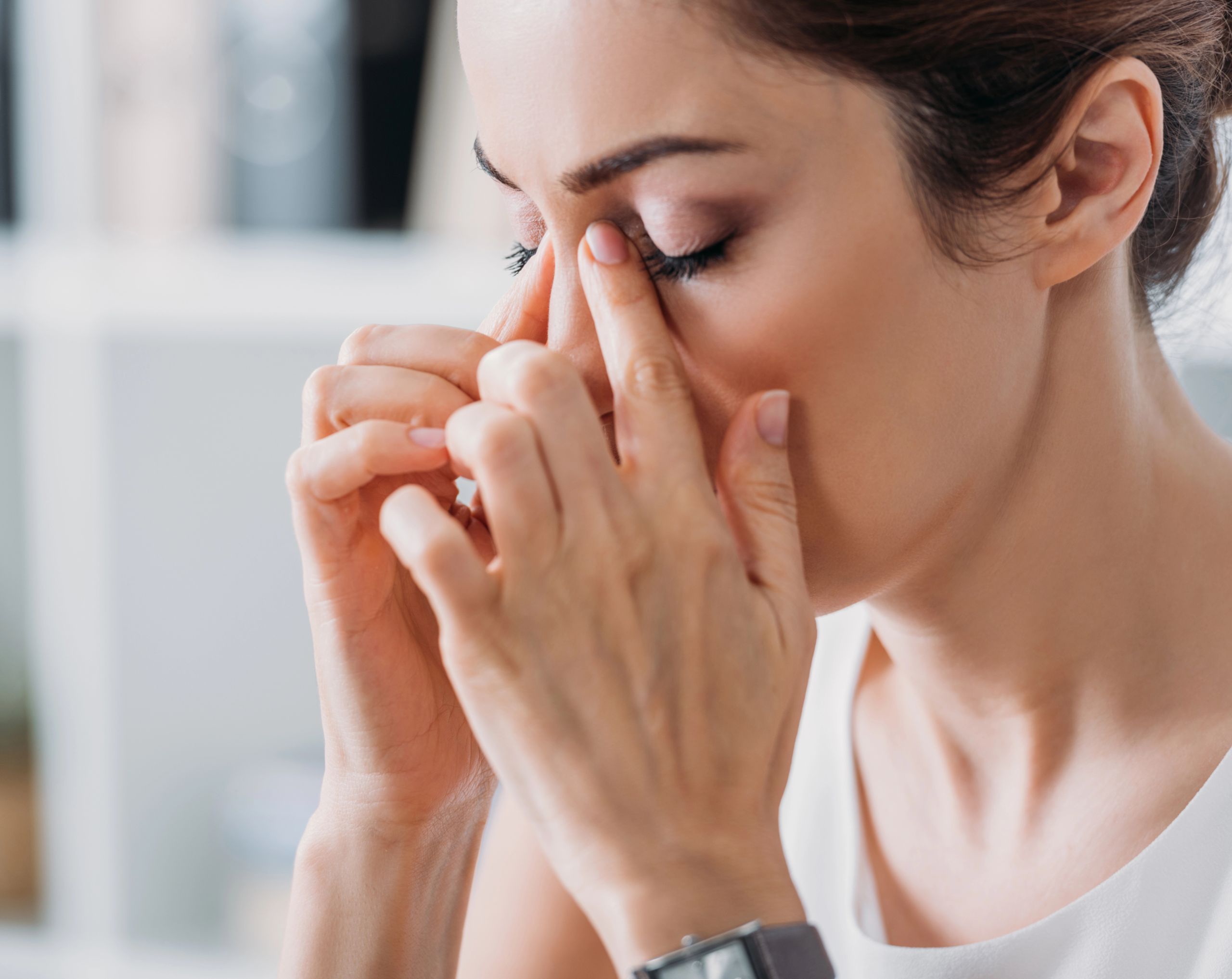 Mujer joven se toca los senos paranasales debido a molestias causadas por la sinusitis.
