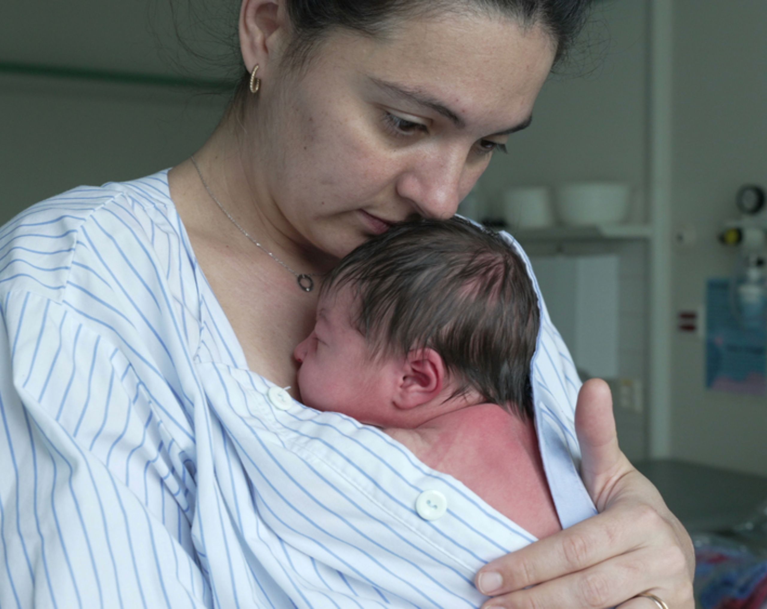 Mamá joven acuna a su bebé recién nacido en brazos tras un parto por cesárea, mostrando cuidado, recuperación postparto y síntomas de posibles complicaciones.