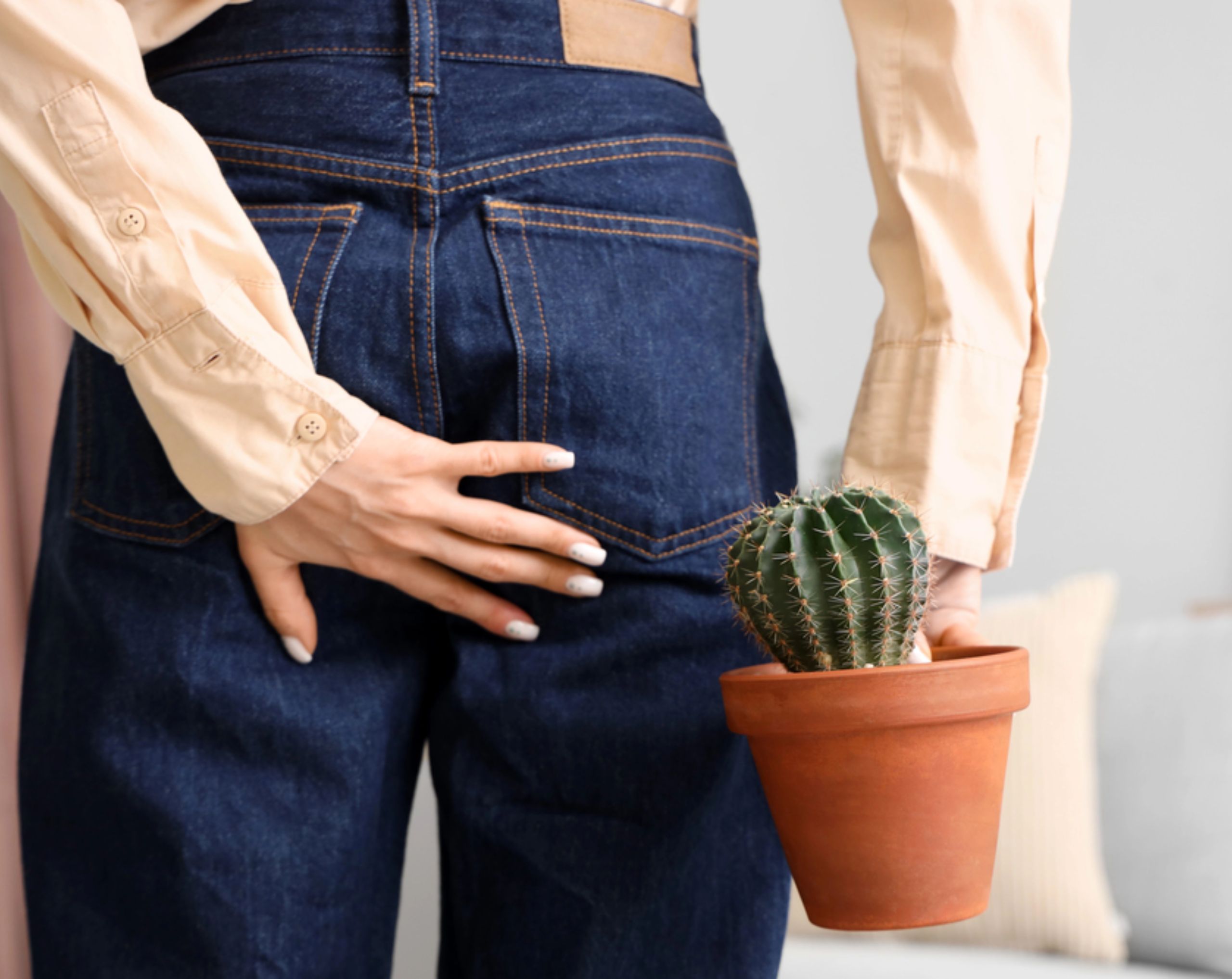 Mujer se encuentra de espaldas tocando su trasero con una de sus manos y sosteniendo un cáctus con la otra como señal de comezón, síntoma de verrugas en el ano.
