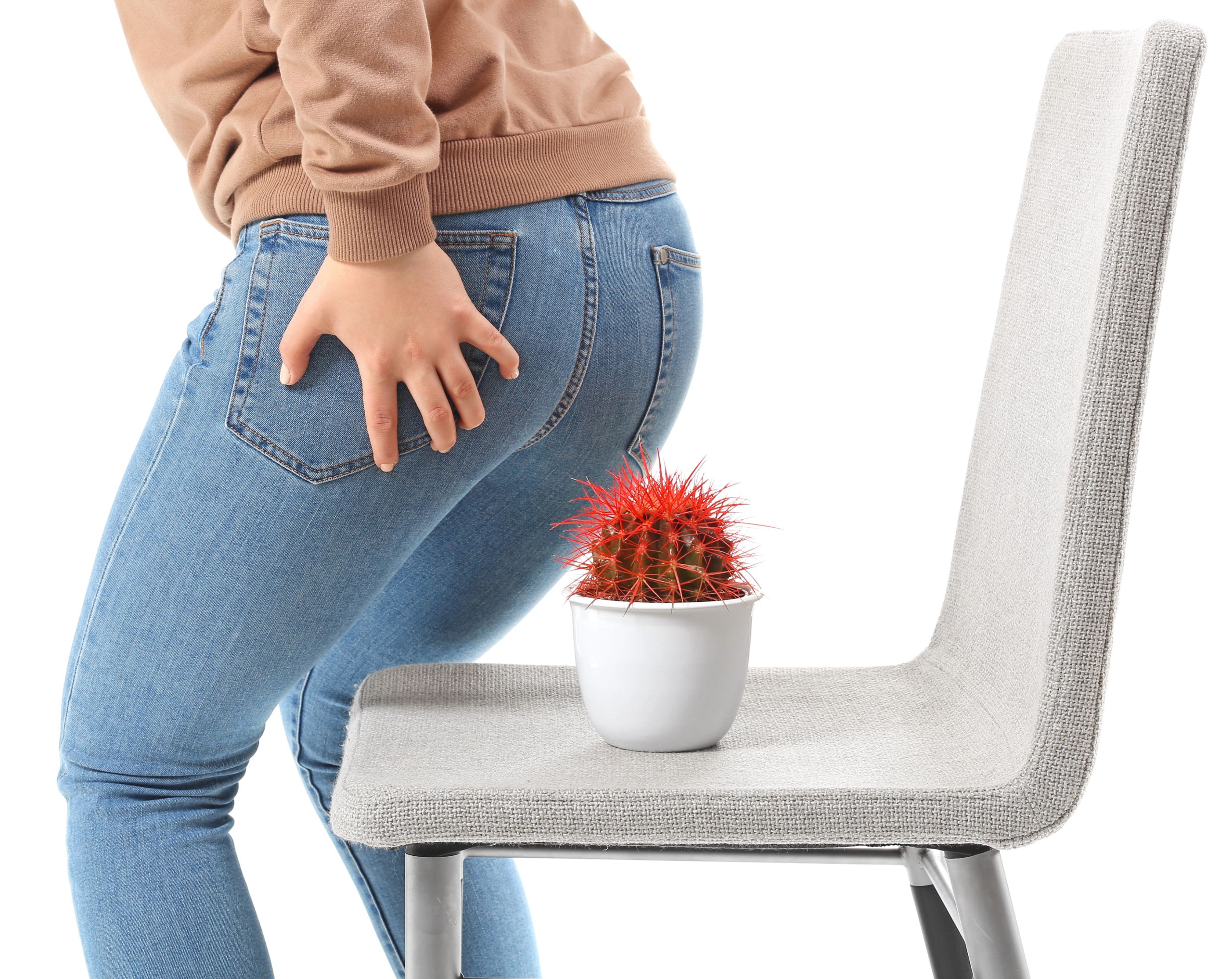 Mujer a punto de sentarse en una silla con un cactus, sosteniendo la zona del ano con una mano, en representación del ardor y comezón causados por las almorranas.