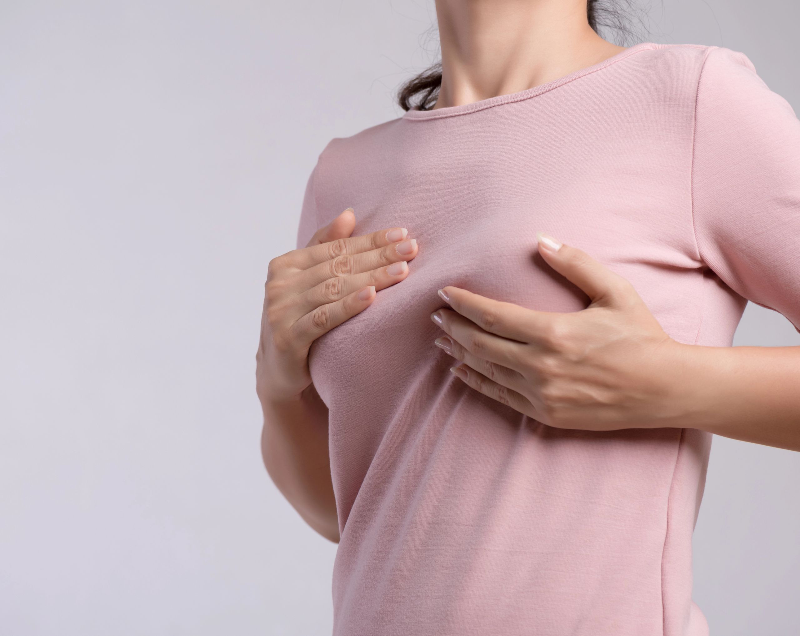 Mujer de mediana edad realizando una autoexploración mamaria con ambas manos para detectar signos tempranos de cáncer de mama.