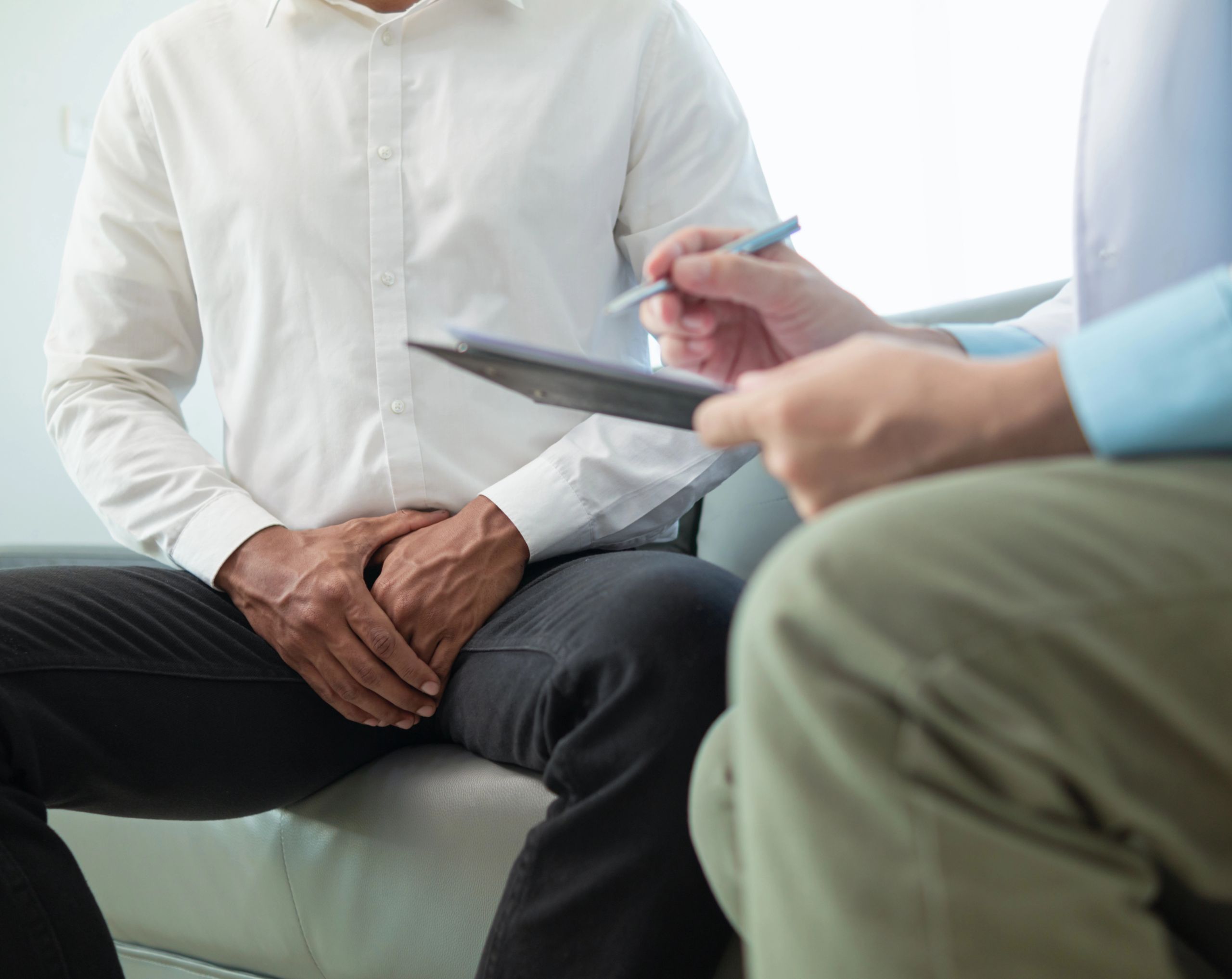 Paciente masculino de mediana edad en consultorio médico, mostrando molestias en la zona testicular mientras el urólogo explica diagnóstico por posible cáncer de testículo.