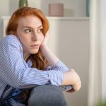 Mujer de mediana edad sentada en un sofá soñando despierta, reflejando ensoñación excesiva.